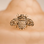 Gold bee-shaped brooch with pearl details on a blurred background