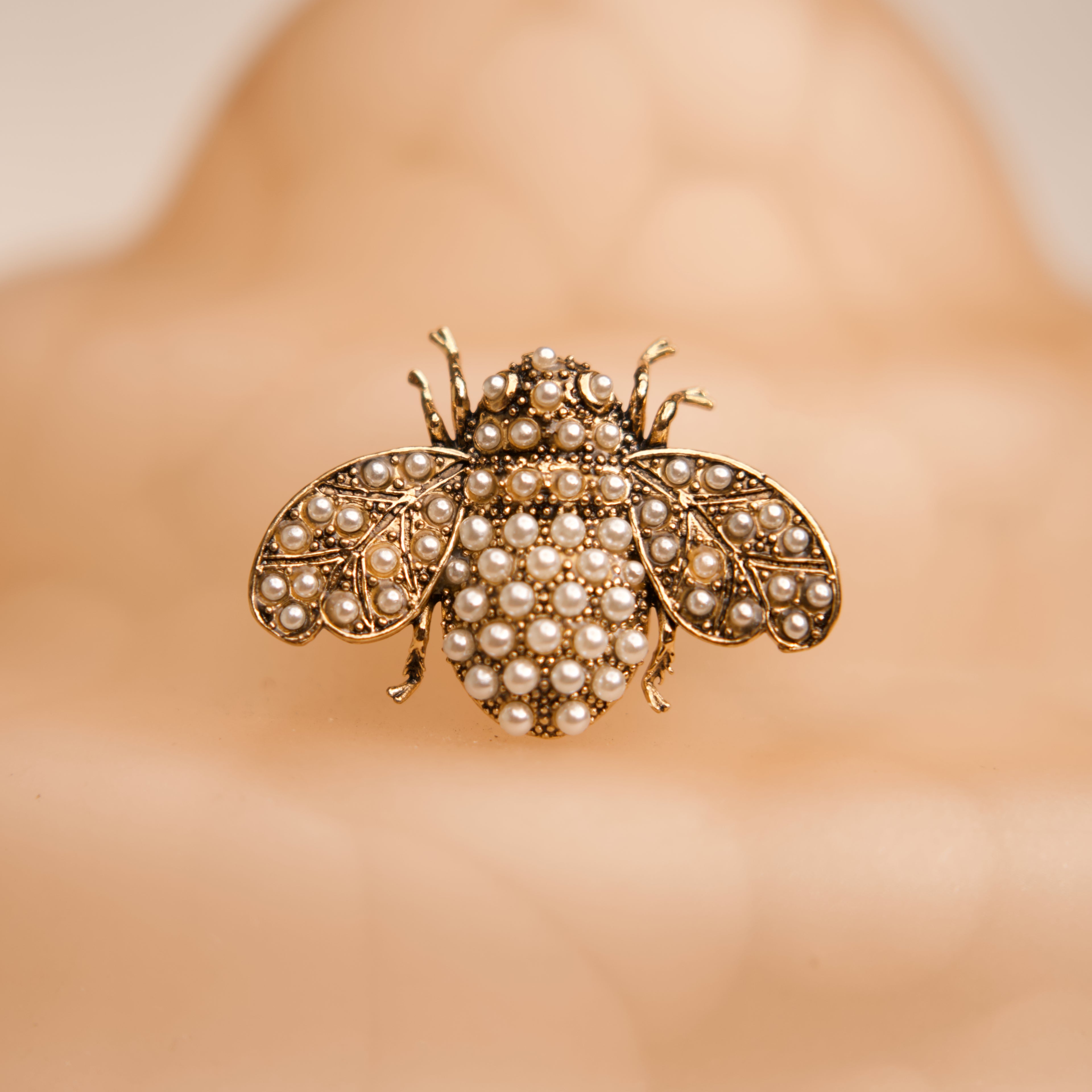 Gold bee-shaped brooch with pearl details on a blurred background
