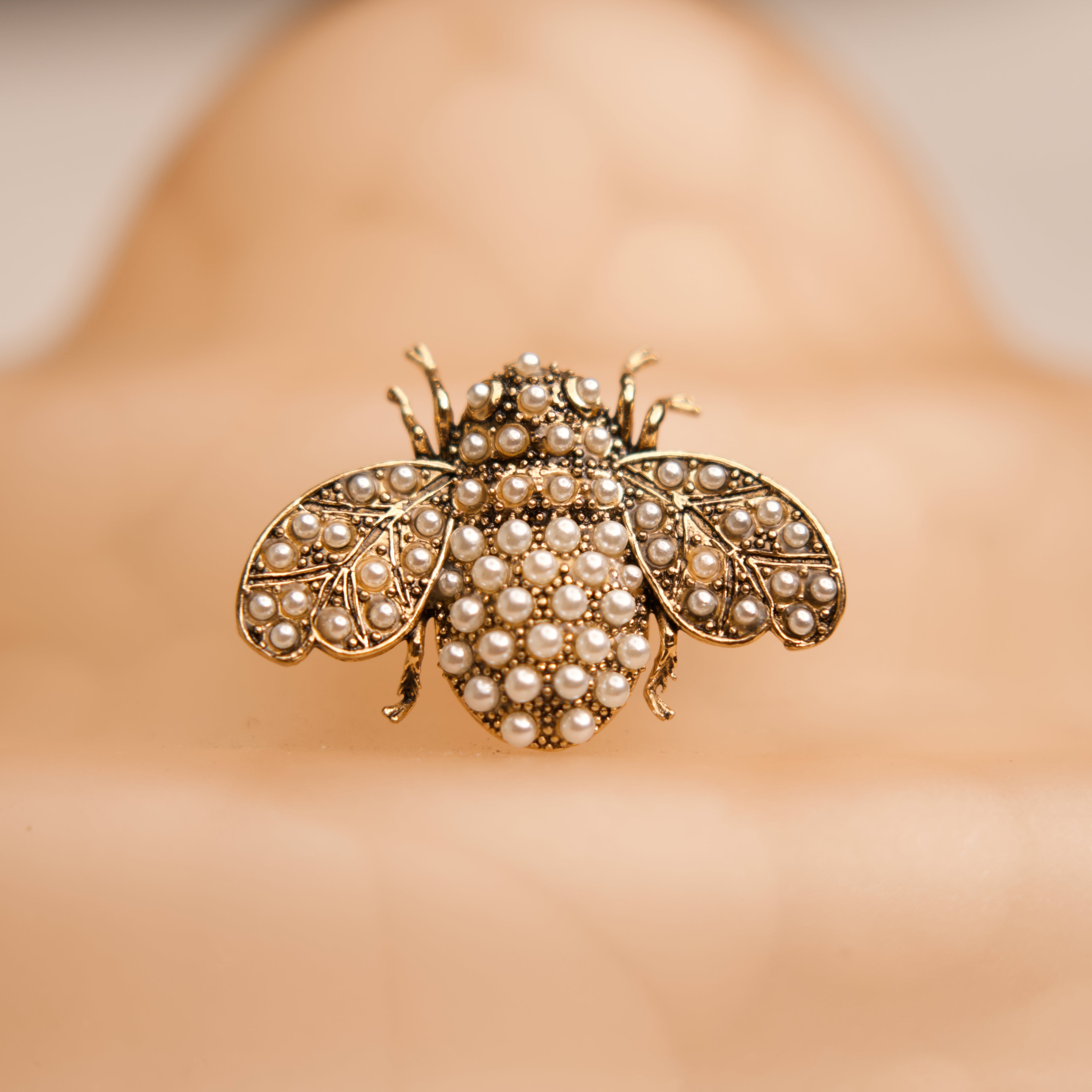 Gold bee-shaped brooch with pearl details on a blurred background