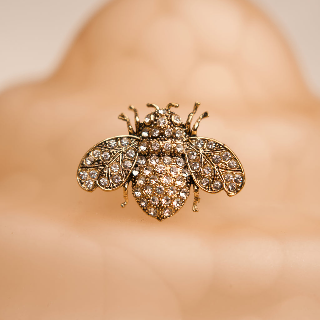 Gold bee-shaped brooch with gemstones on a blurred background