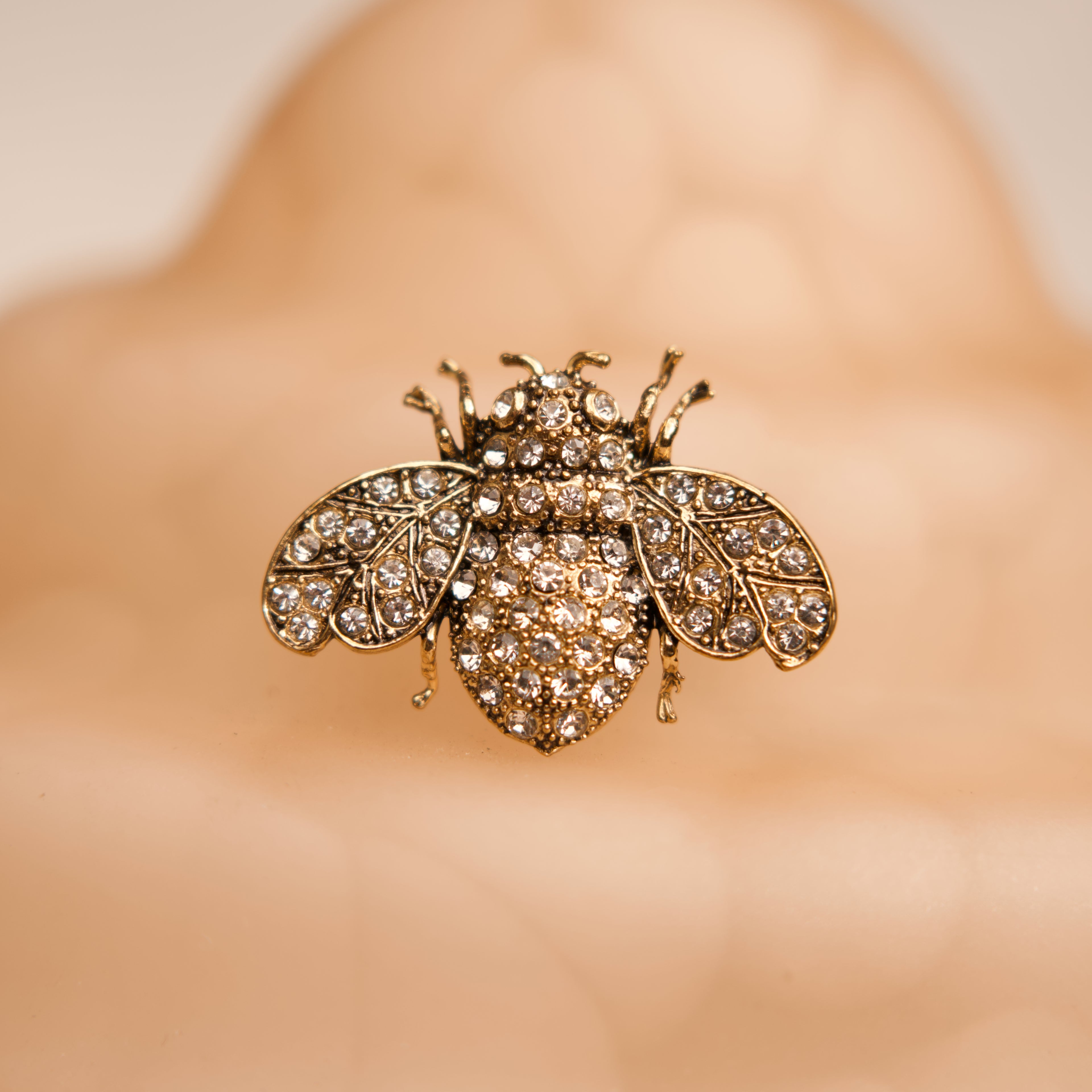 Gold bee-shaped brooch with gemstones on a blurred background