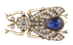 Gold insect-shaped brooch with blue gem and clear stones on a white background