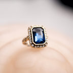 Gold ring with a blue gemstone on a blurred background