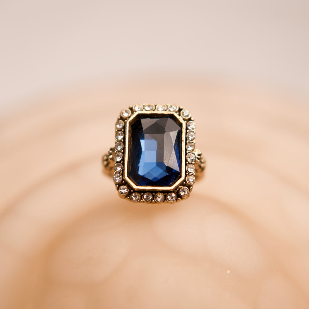 Gold ring with a blue gemstone on a beige background