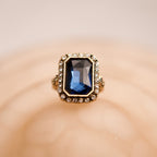 Gold ring with a blue gemstone on a beige background