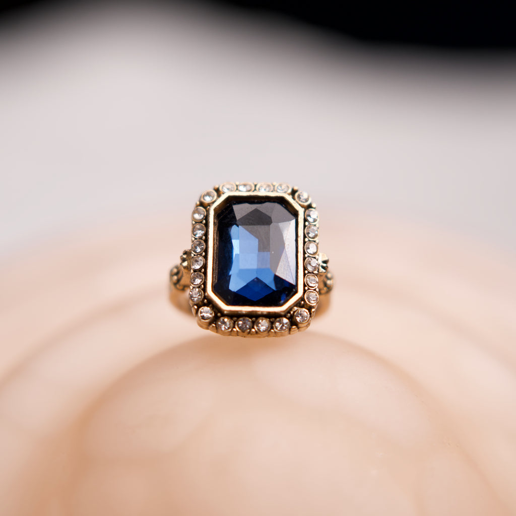 Gold ring with a blue gemstone on a soft beige background