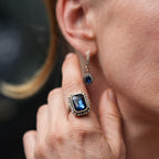 Close-up of a person wearing a blue gemstone ring and earring.