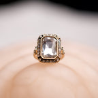 Gold ring with a large central gemstone on a soft beige background