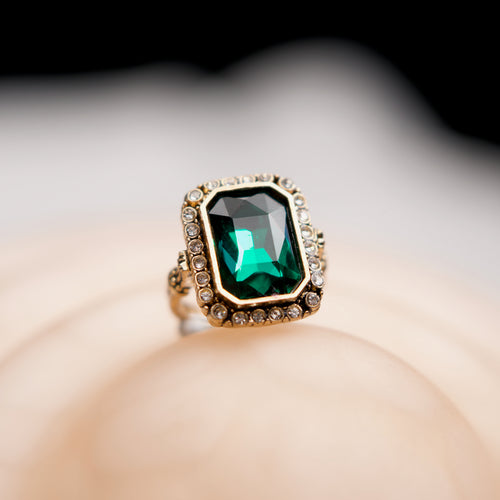 Gold ring with a green gemstone on a neutral background