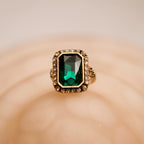 Gold ring with a green gemstone on a beige background
