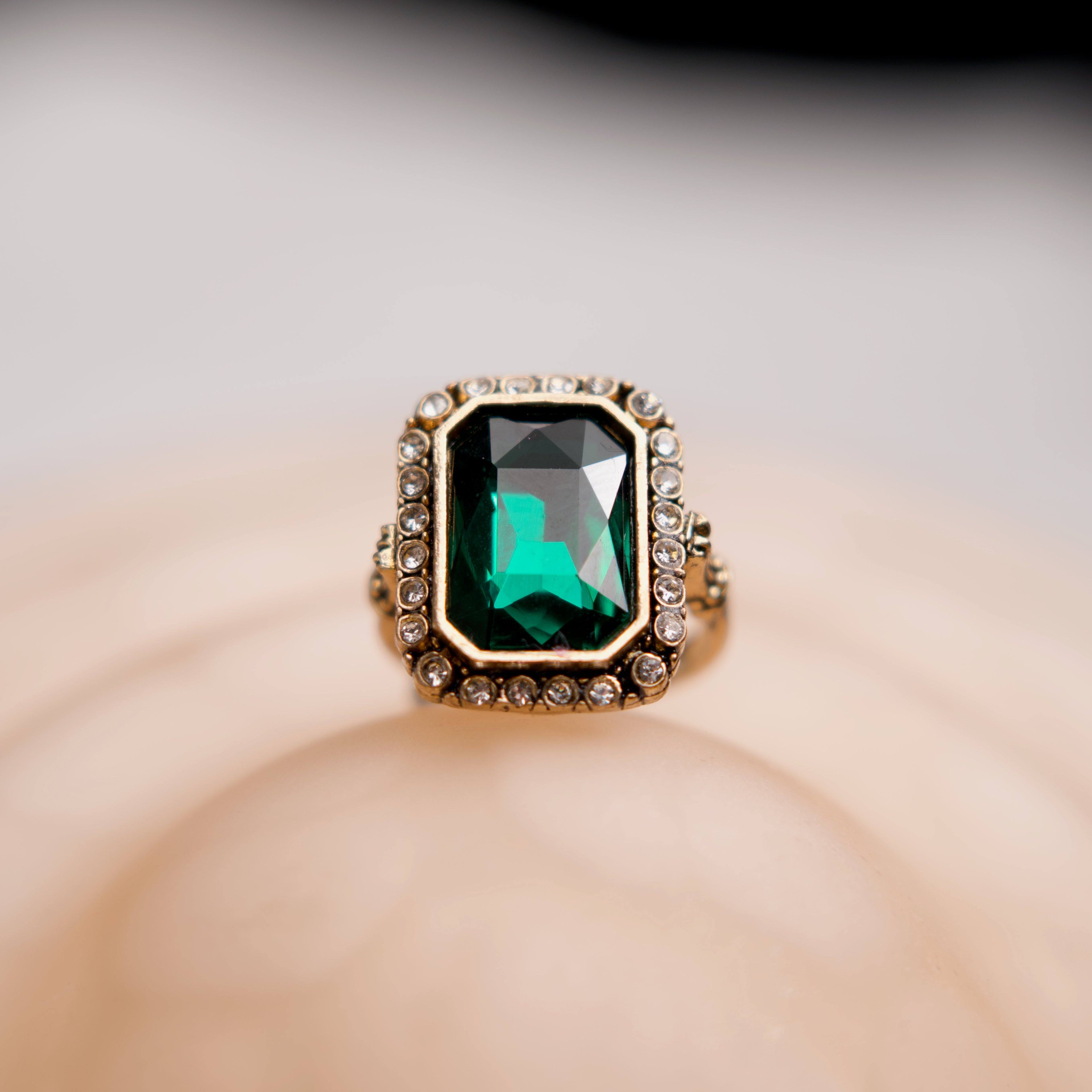Ring with a green gemstone and gold accents on a soft beige background