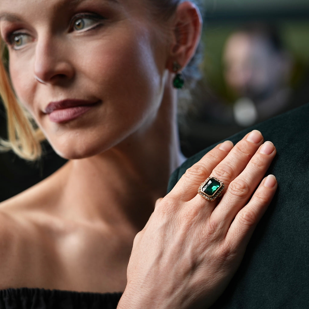 Woman wearing a ring with an emerald stone on a blurred background