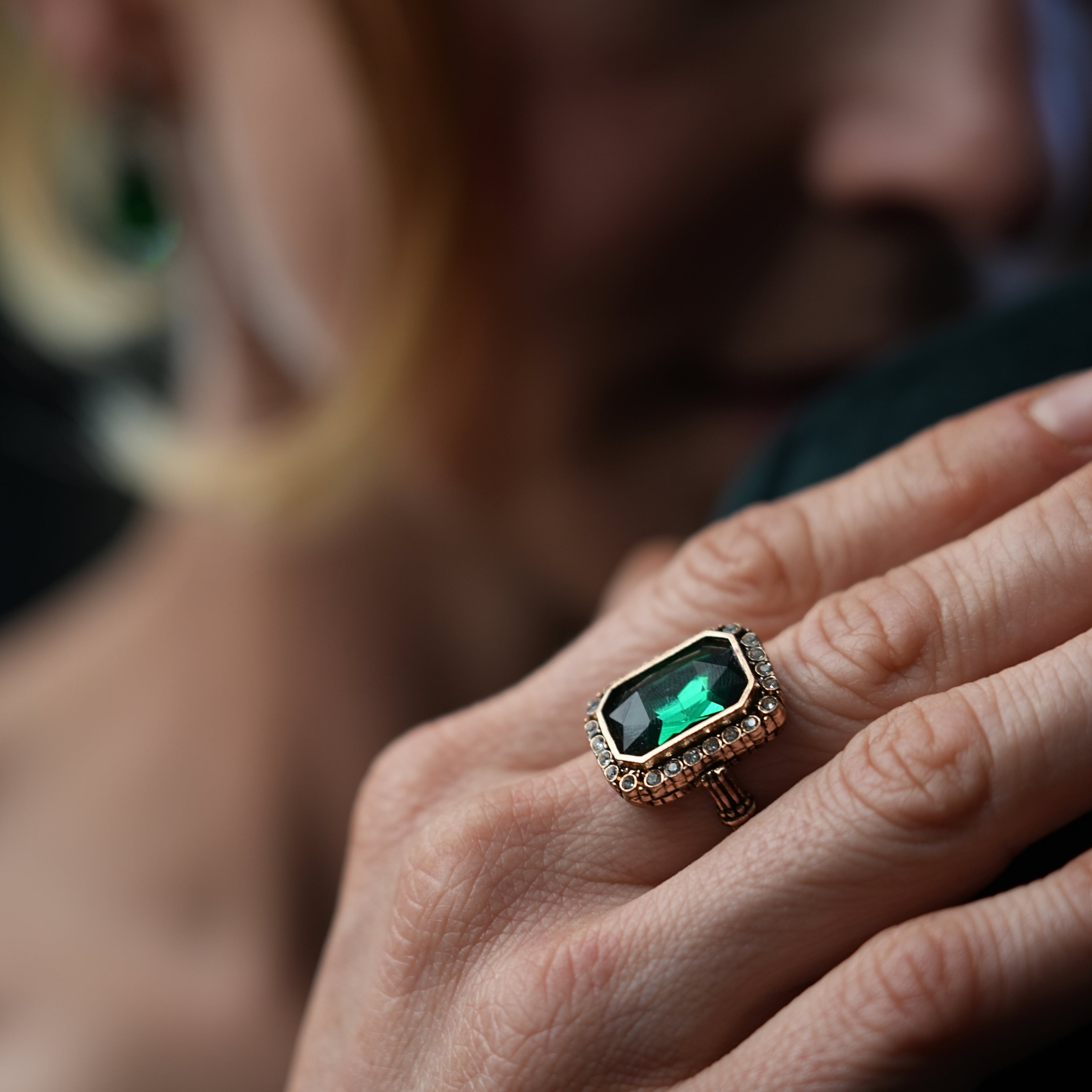 Close-up of a hand wearing a ring with a green gemstone, blurred background