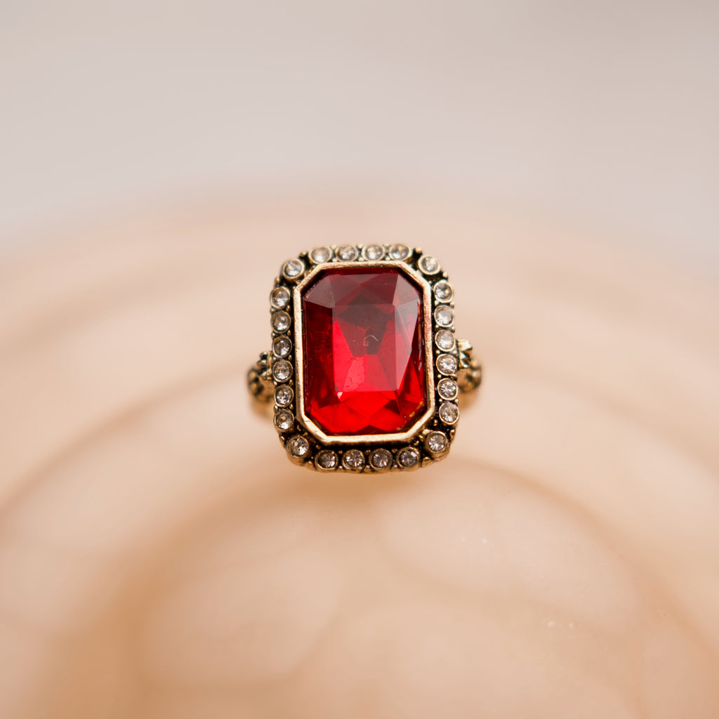 Ring with a red gemstone and gold border on a beige background