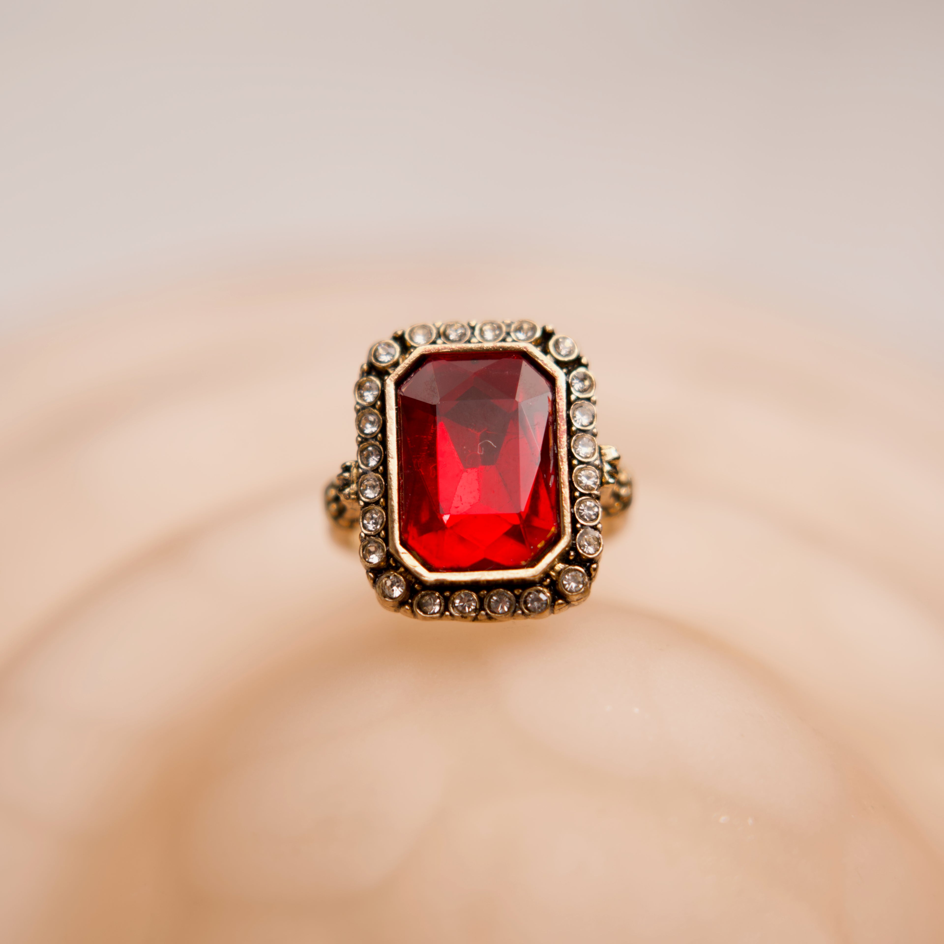 Ring with a red gemstone and gold border on a beige background