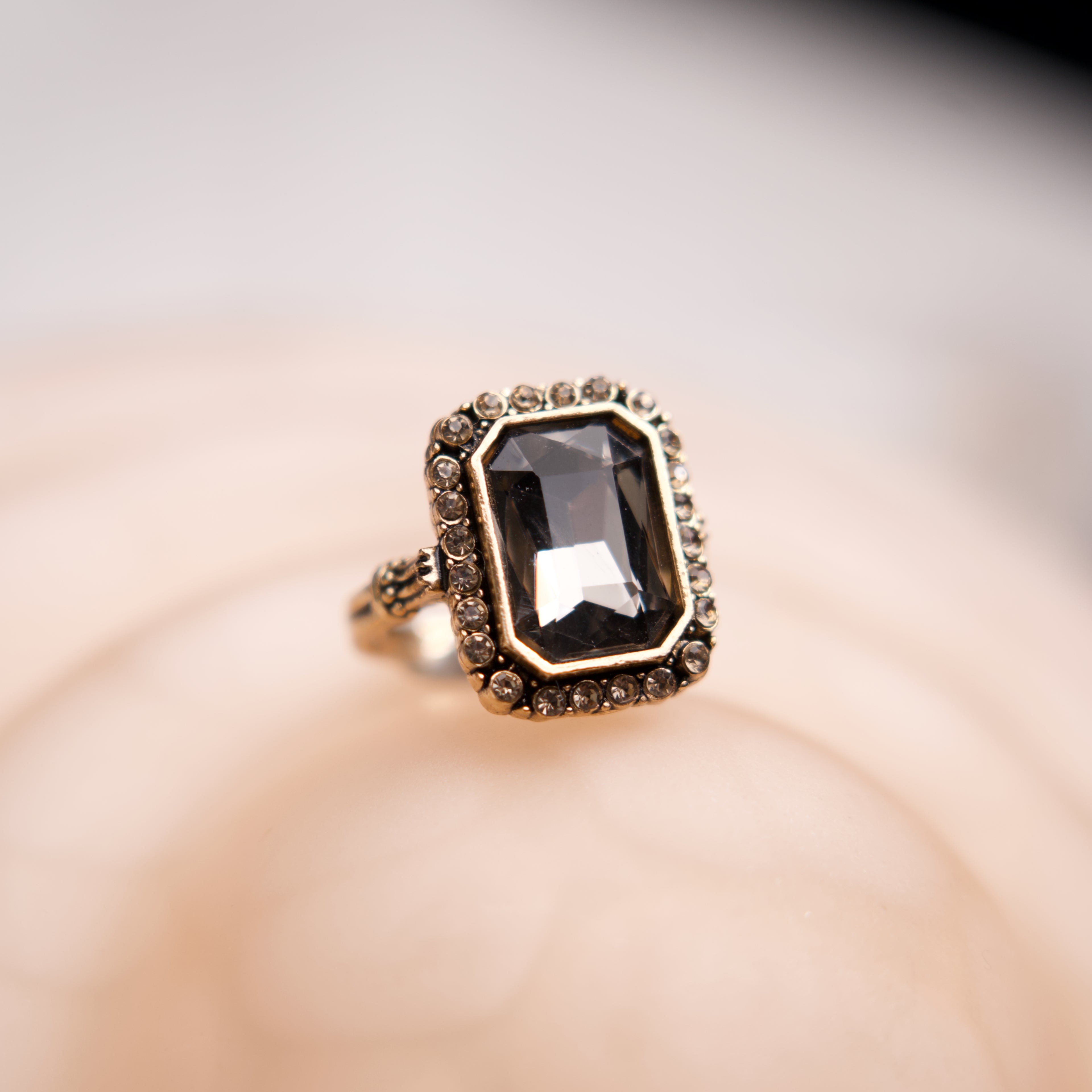 Gold ring with a large black gemstone on a soft pink background