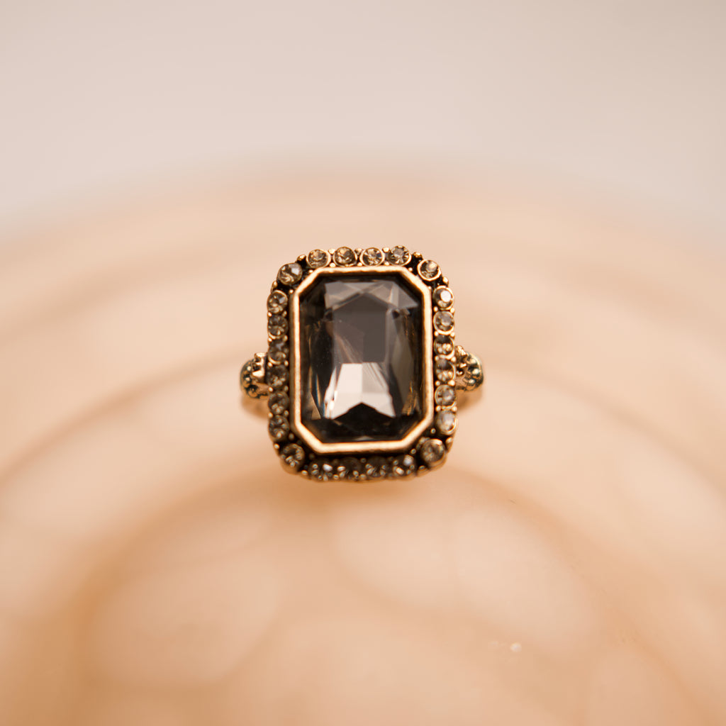 Gold ring with a dark gemstone on a beige background
