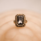 Gold ring with a dark gemstone on a beige background