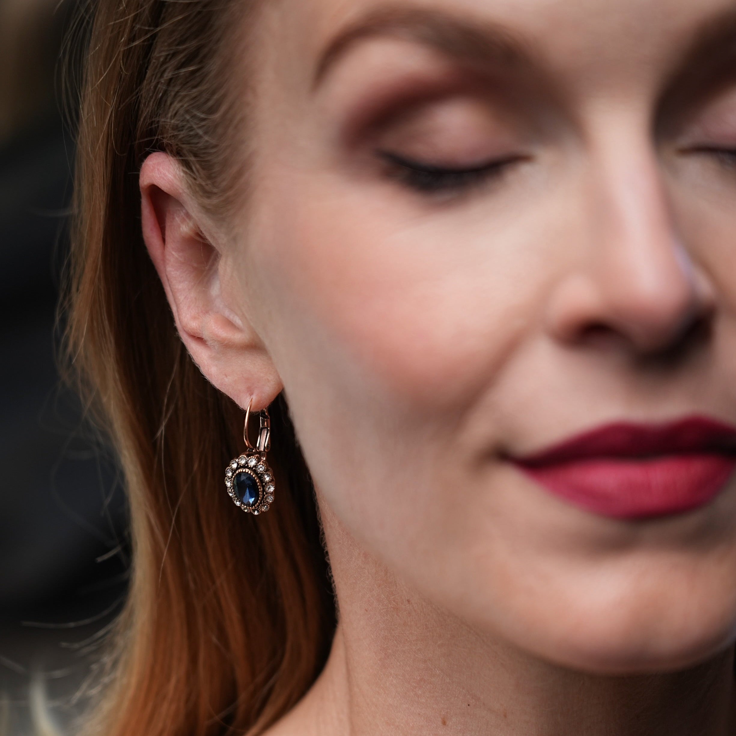 Close-up of a woman wearing an earring with a dark gemstone against a blurred background