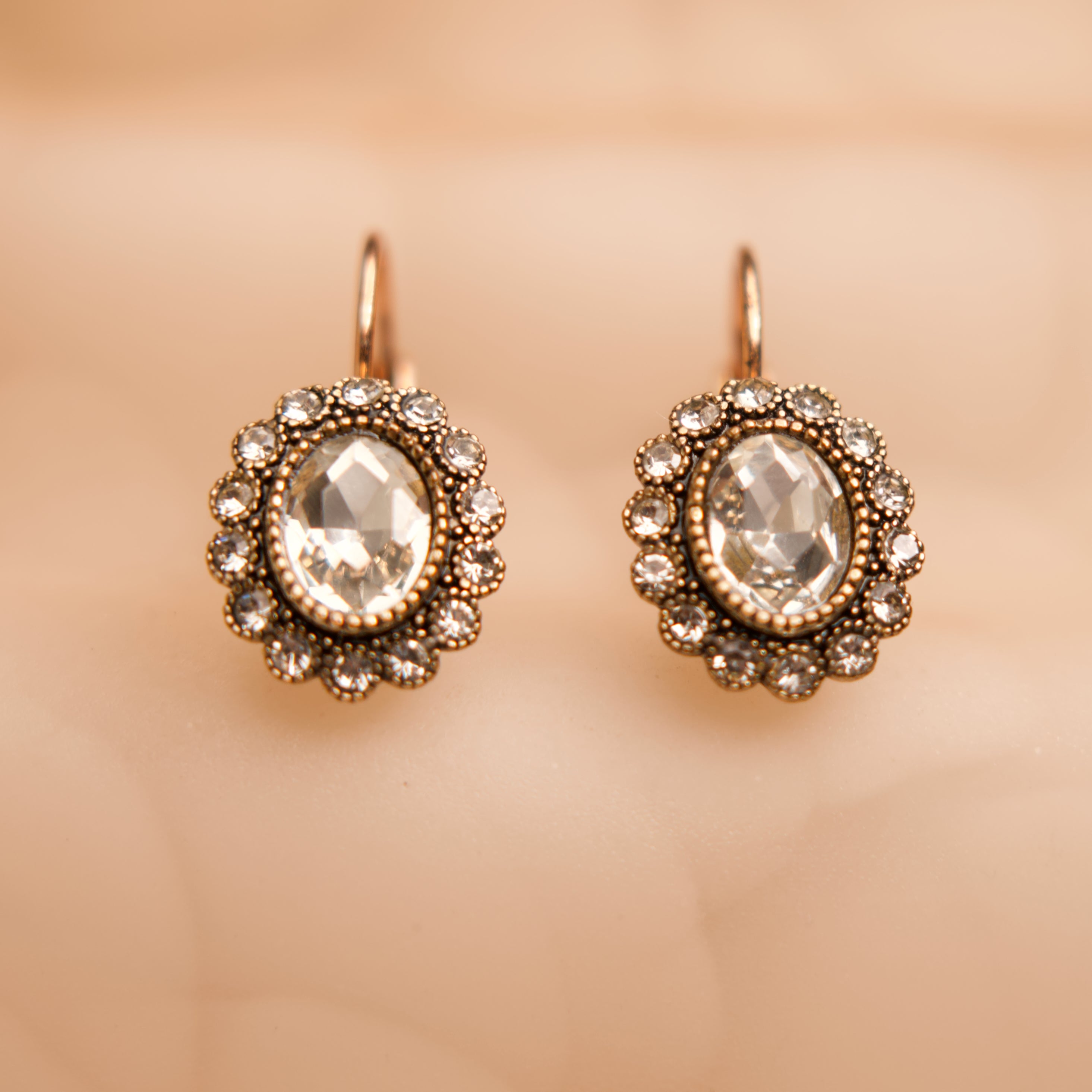 Pair of ornate earrings with clear gemstones on a beige background
