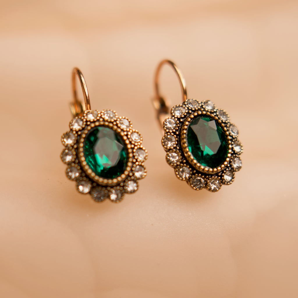 Pair of gold earrings with green gemstones on a beige background