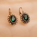 Pair of gold earrings with green gemstones on a beige background