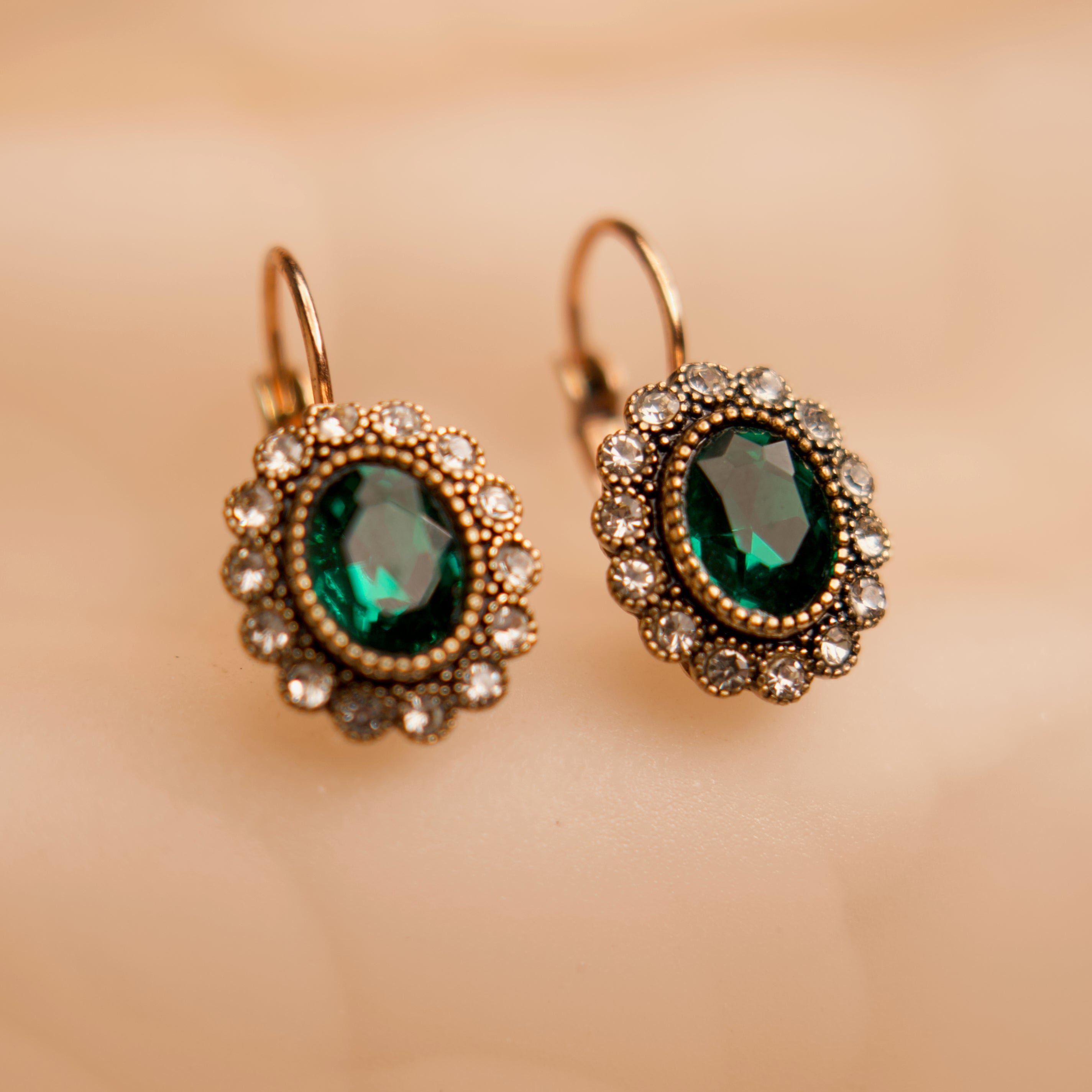 Pair of gold earrings with green gemstones on a beige background