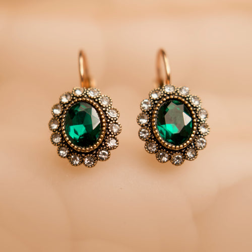 Pair of earrings with green gemstones and gold accents on a beige background