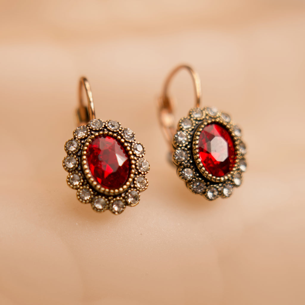 Pair of earrings with red gemstones and gold accents on a beige background