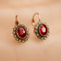Pair of earrings with red gemstones and gold accents on a beige background
