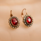 Pair of earrings with red gemstones and gold accents on a beige background