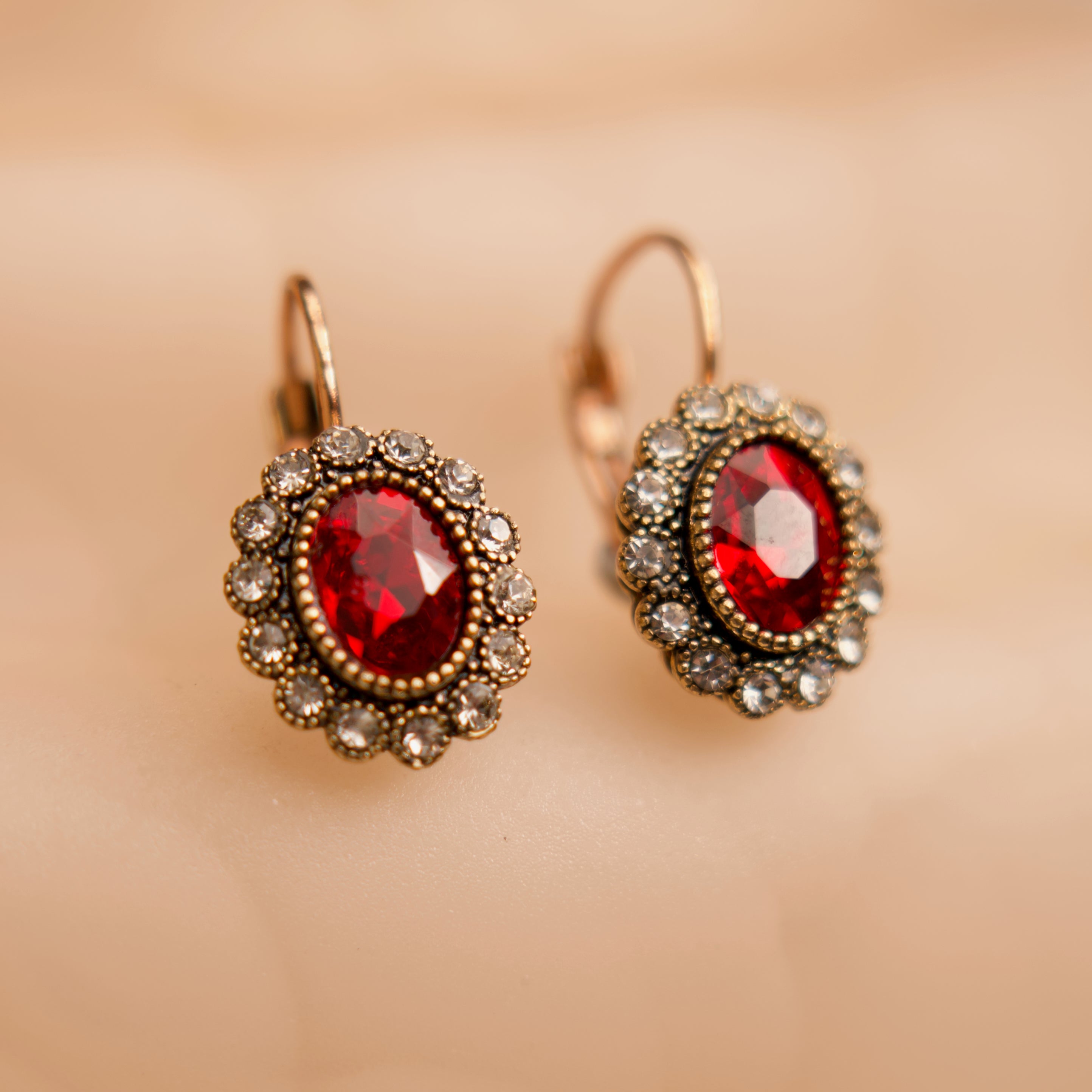 Pair of earrings with red gemstones and gold accents on a beige background