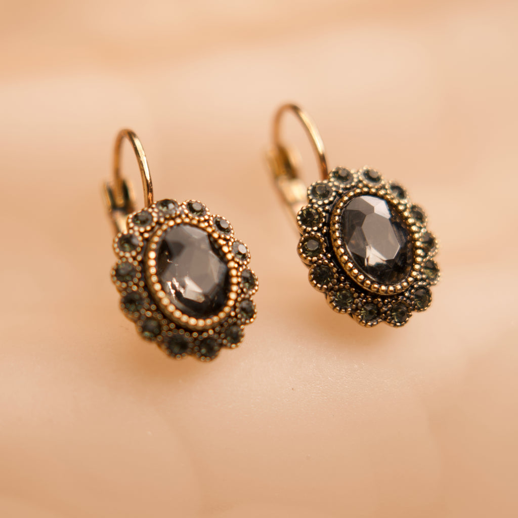 Pair of gold earrings with dark gemstones on a beige background