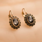 Pair of gold earrings with dark gemstones on a beige background