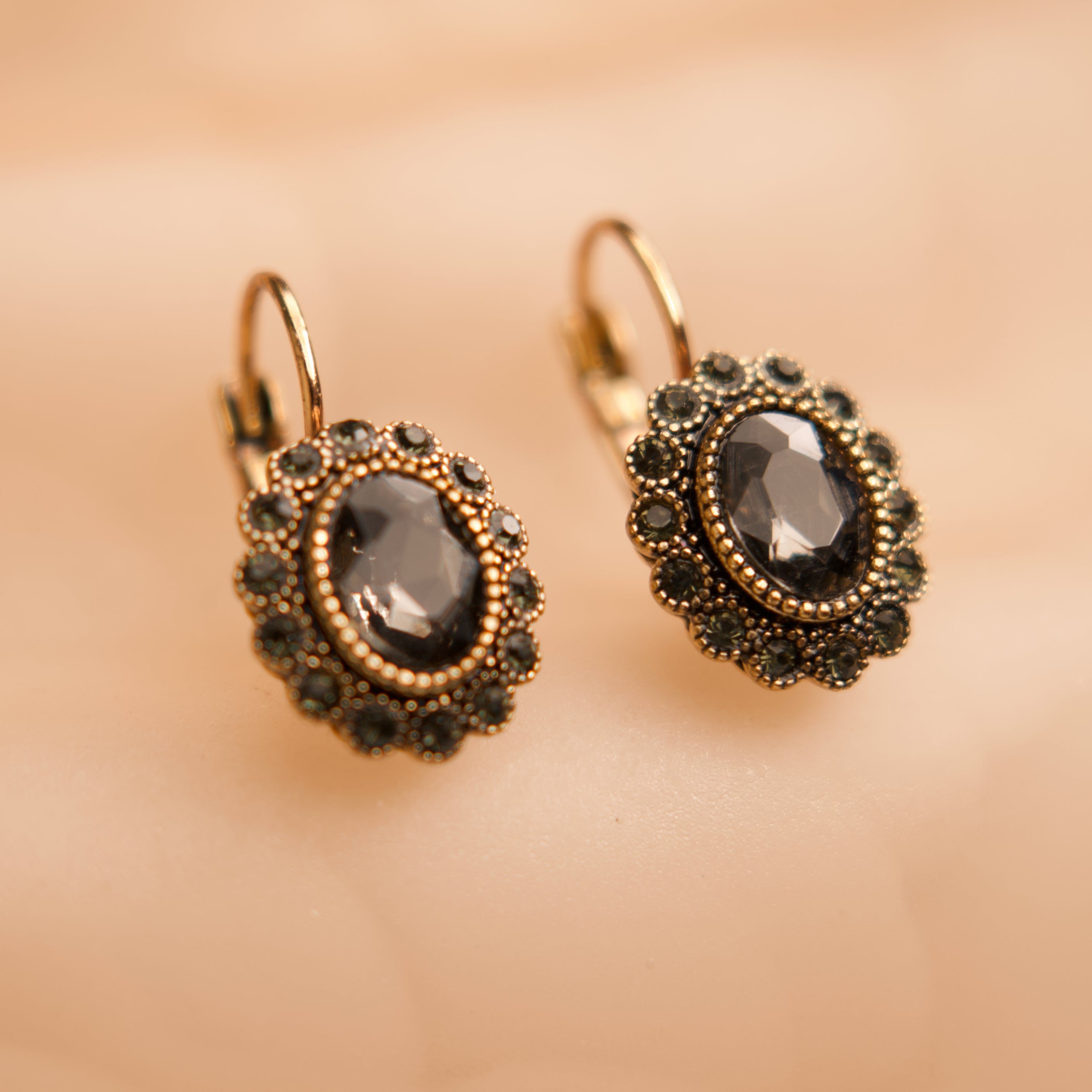 Pair of gold earrings with dark gemstones on a beige background