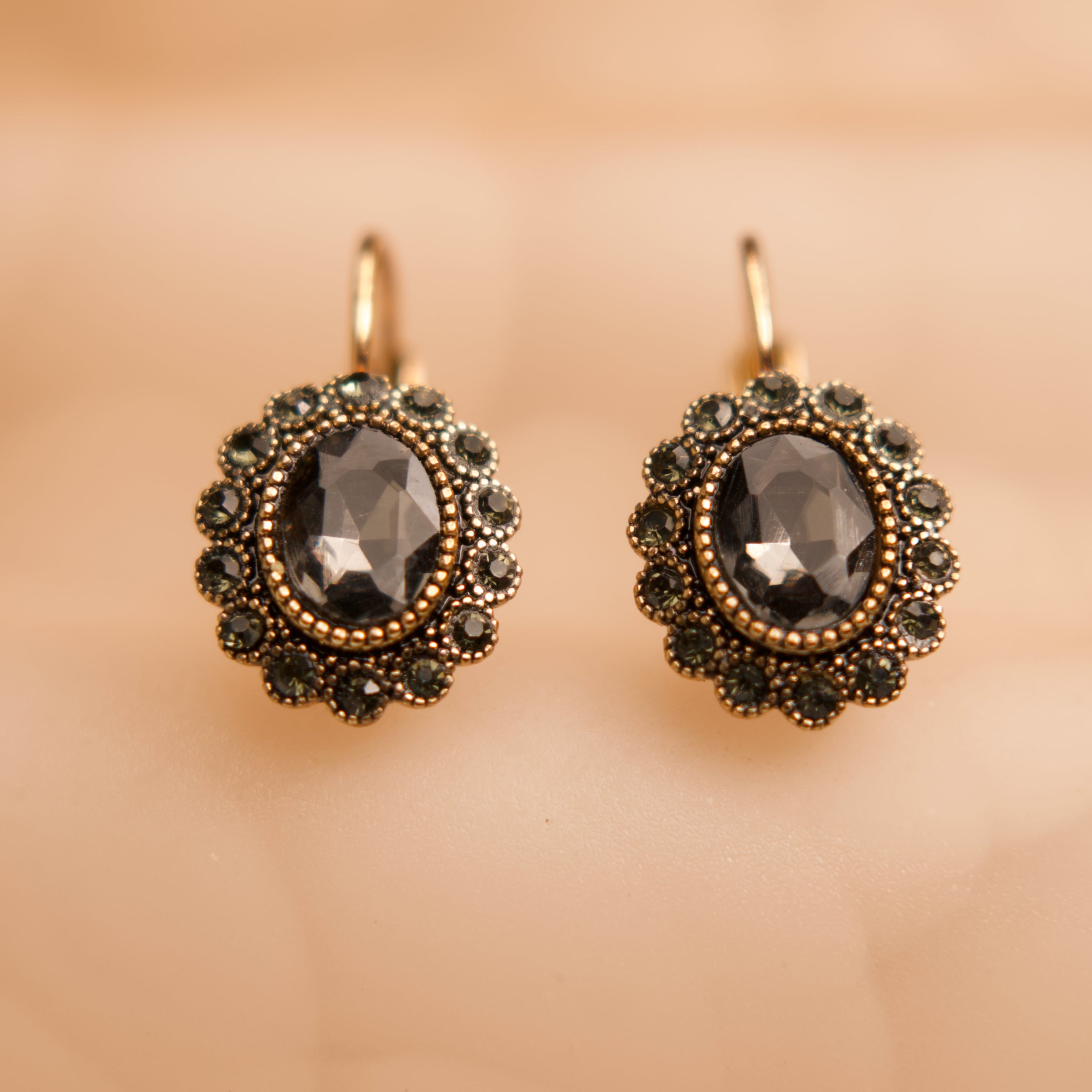 Pair of ornate earrings with dark gemstones on a beige background