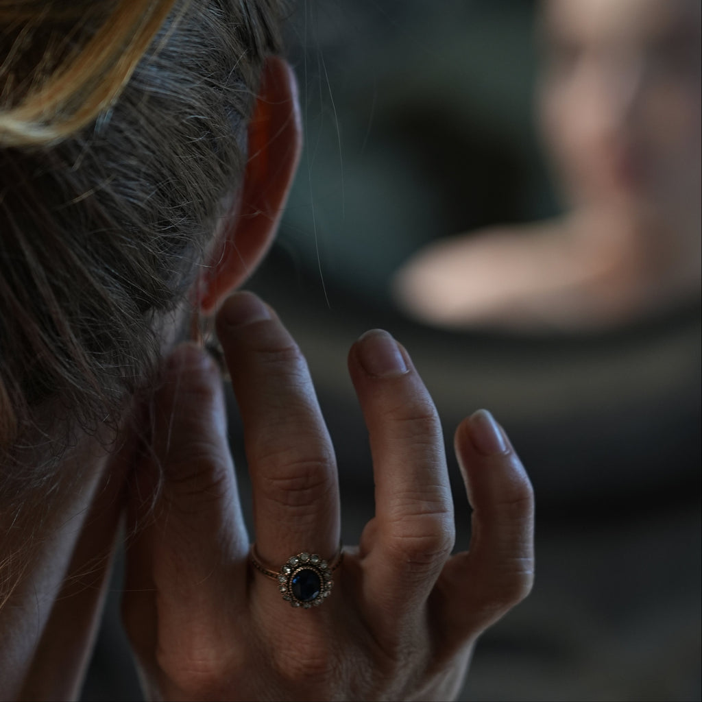 Close-up of a hand with a ring touching an ear, with a blurred background
