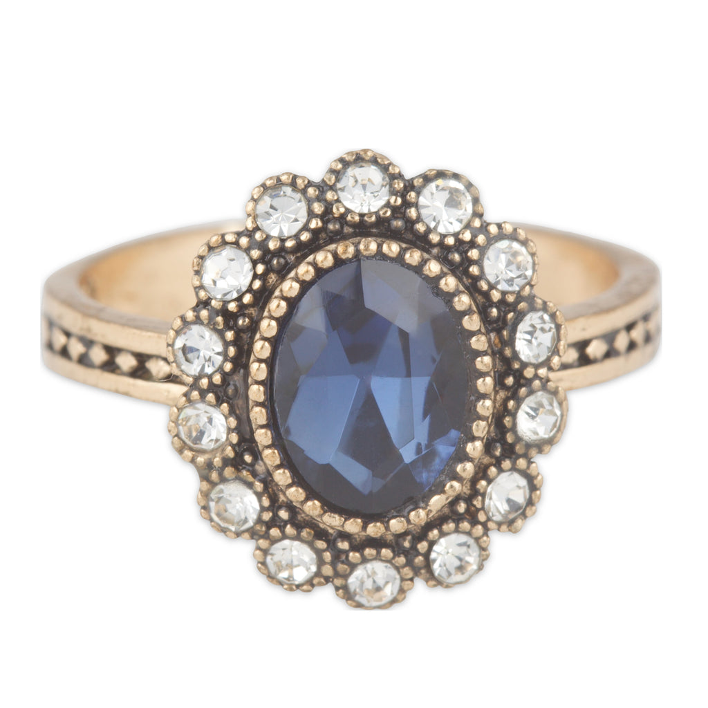 Gold ring with a blue gemstone and clear stones on a white background