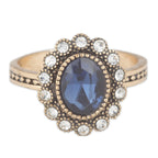 Gold ring with a blue gemstone and clear stones on a white background