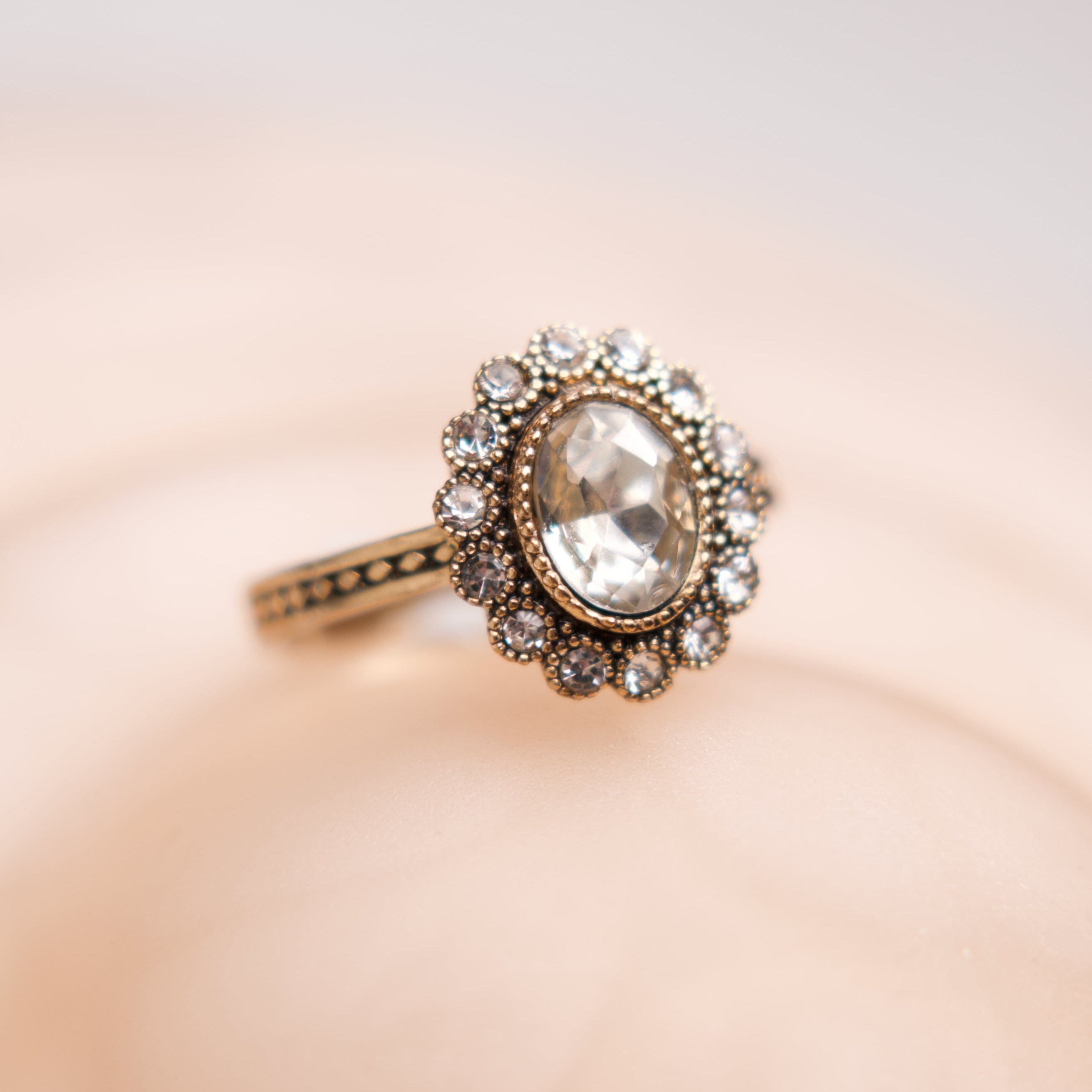 Elegant ring with a large central gemstone on a soft pink background