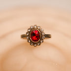 Gold ring with a red gemstone on a beige background