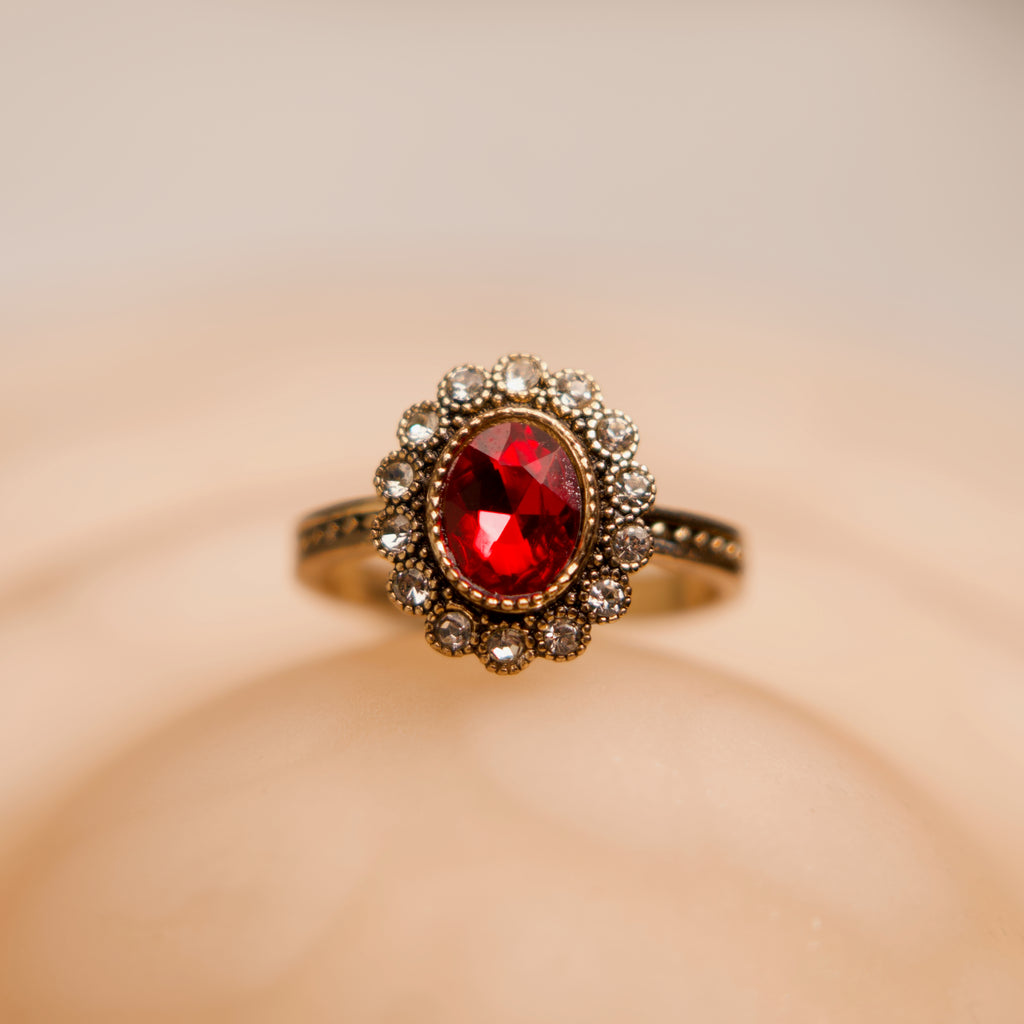 Gold ring with a red gemstone on a beige background