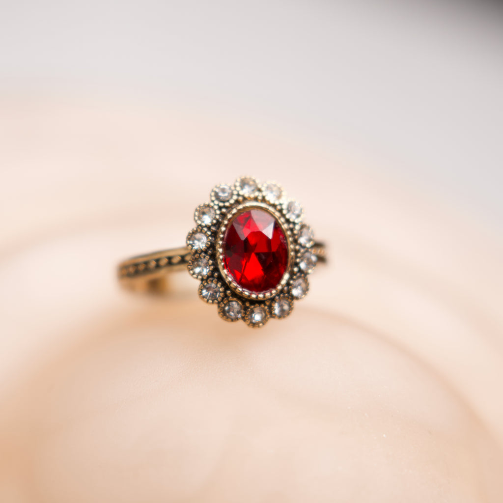 Ring with a red gemstone and gold accents on a soft pink background