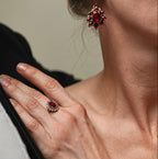 Close-up of a woman wearing red gemstone earrings and ring, with a neutral background.
