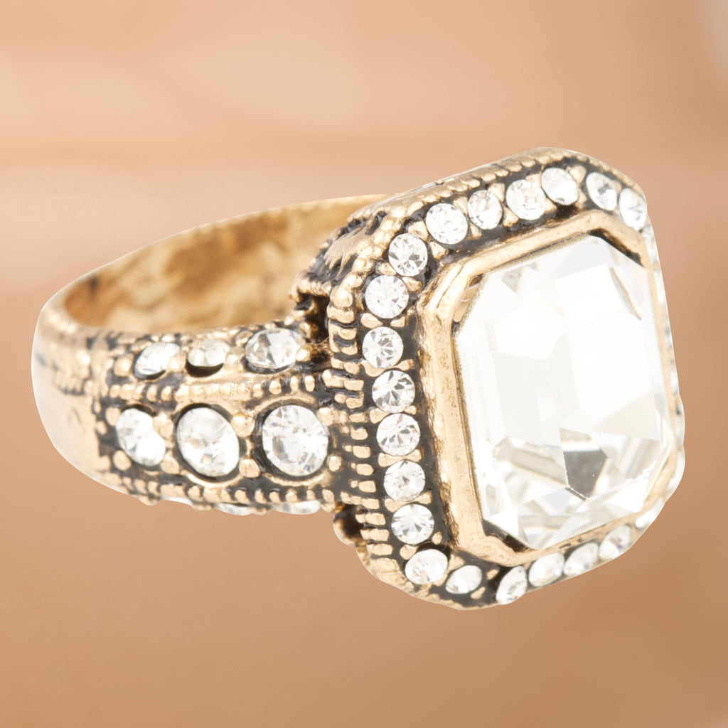 Gold ring with a large central gemstone and smaller stones on a beige background