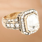Gold ring with a large central gemstone and smaller stones on a beige background