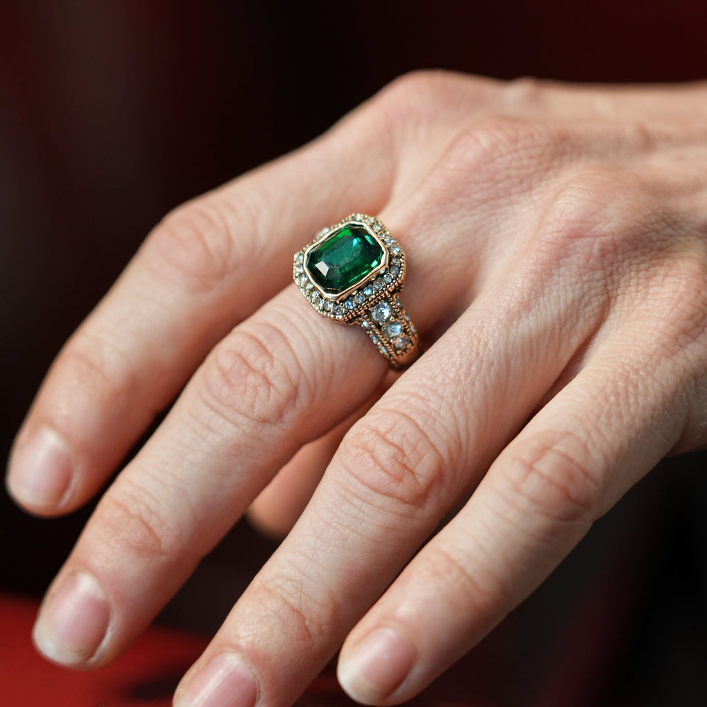Close-up of a hand wearing an emerald ring on a red surface