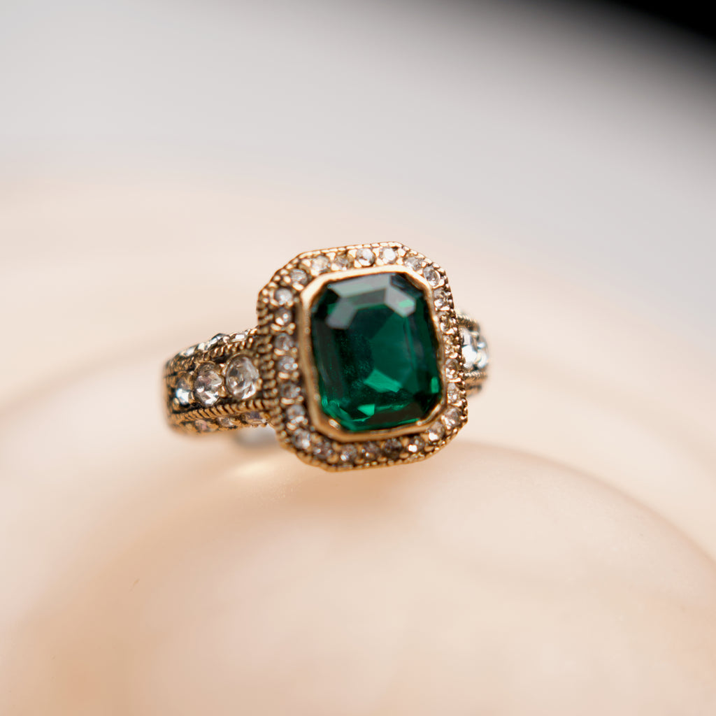 Gold ring with a green gemstone on a beige background