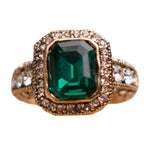 Gold ring with a green gemstone and diamond accents on a white background