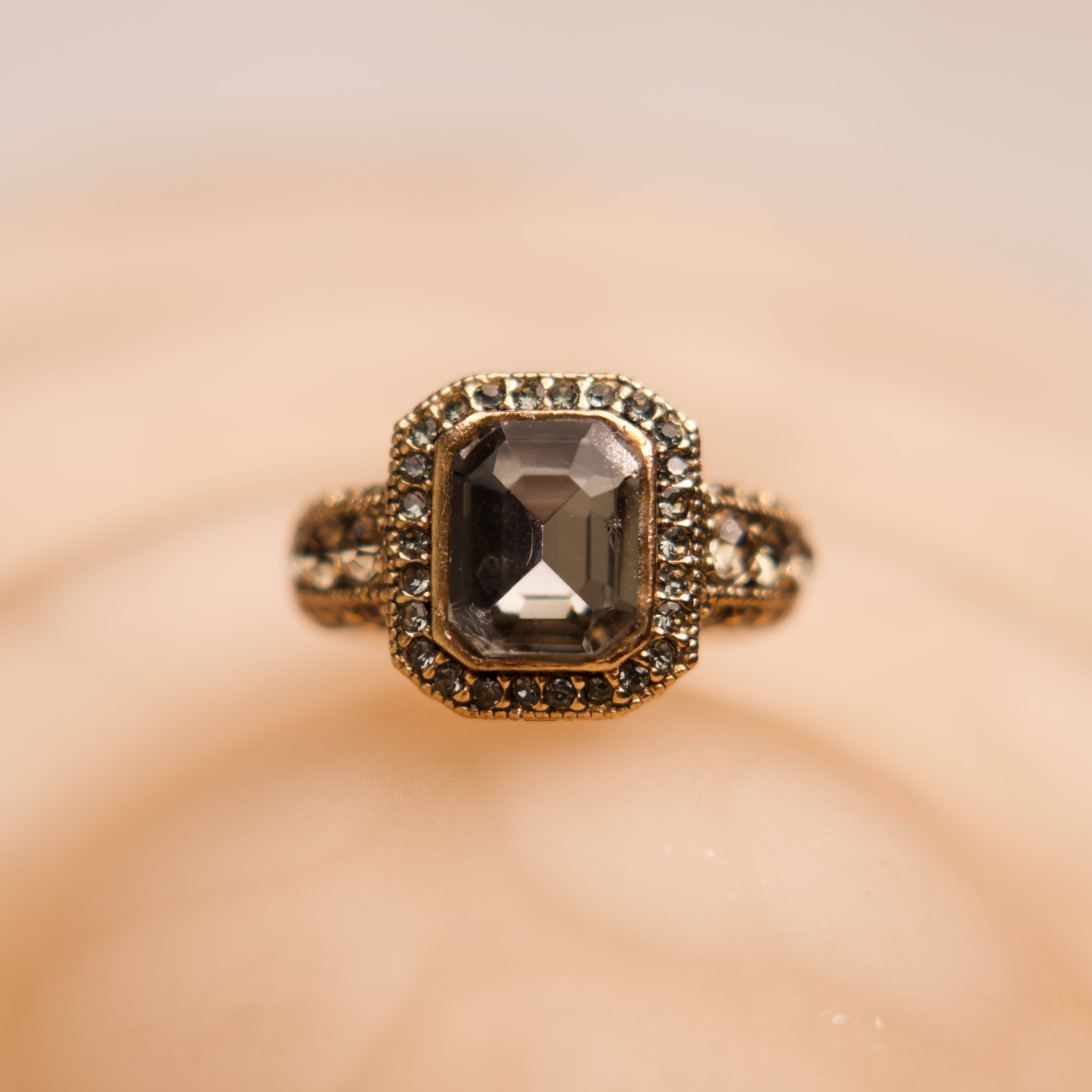 Gold ring with a central gemstone on a soft beige background